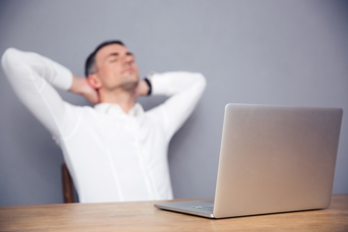 Tired businessman sitting at the table with laptop in office. Focus on laptop